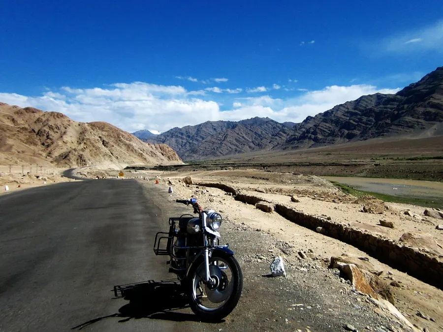 A Royal Enfield motorcycle parked on an empty mountain highway under a blue sky